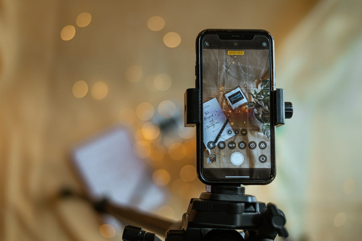 Smartphone auf einem Stativ filmt einen Schreibtisch-Aufbau für Social-Media-Content, dahinter warmes Bokeh-Licht