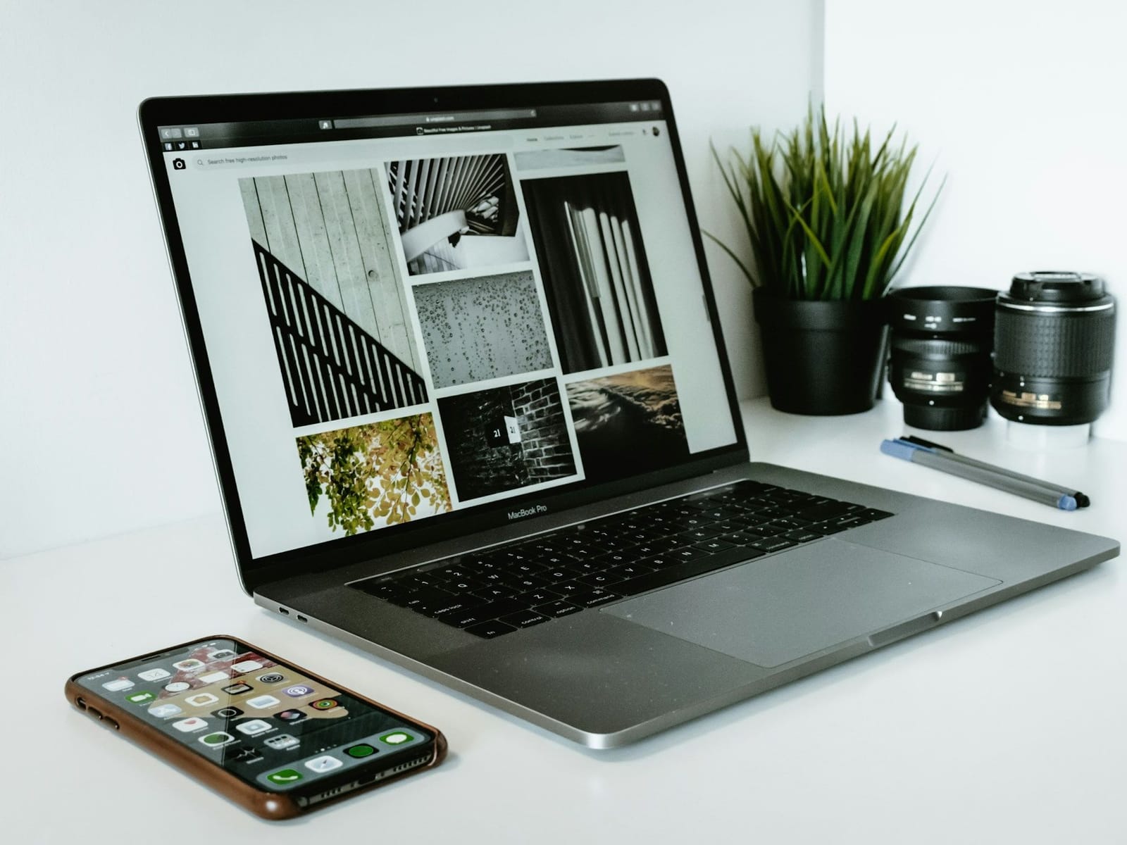 Laptop mit geöffneter Portfolio-Website im Bildraster auf weißem Tisch, davor ein Smartphone, daneben Objektive und Pflanze
